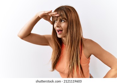 Hispanic Woman With Bang Hairstyle Standing Over Isolated Background Very Happy And Smiling Looking Far Away With Hand Over Head. Searching Concept. 