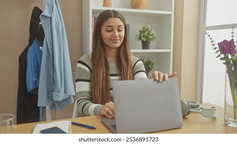 Hispanic woman closing laptop in a modern home interior with casual attire and a striped sweater. - Powered by Shutterstock