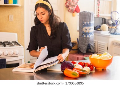 Hispanic woman cooking with recipe book - Young woman preparing vegetables for healthy food at home