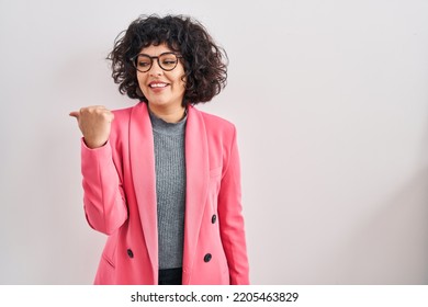 Hispanic Woman With Curly Hair Standing Over Isolated Background Smiling With Happy Face Looking And Pointing To The Side With Thumb Up. 