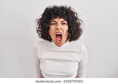 Hispanic woman with curly hair standing over isolated background angry and mad screaming frustrated and furious, shouting with anger. rage and aggressive concept.  - Shutterstock ID 2318759393