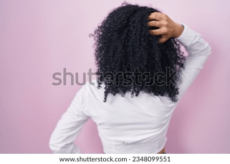 Hispanic woman with curly hair standing over pink background backwards thinking about doubt with hand on head 