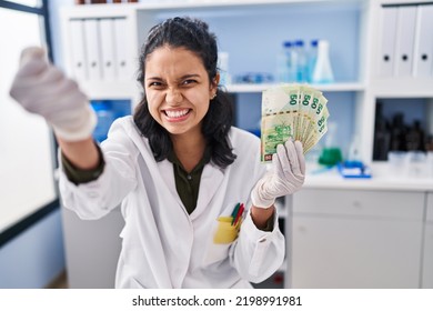 Hispanic Woman With Dark Hair Working At Scientist Laboratory Holding Money Annoyed And Frustrated Shouting With Anger, Yelling Crazy With Anger And Hand Raised 