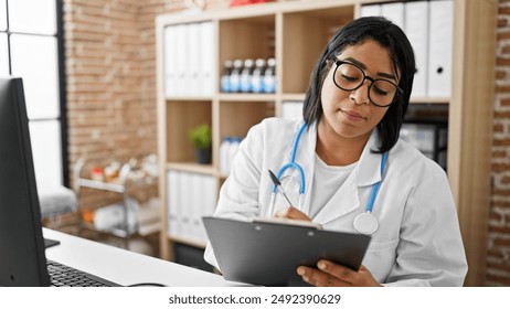 Hispanic woman doctor reviewing medical records on a clipboard in a modern clinic office. - Powered by Shutterstock