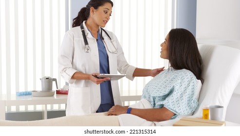 Hispanic Woman Doctor Talking To Patient In Hospital Bed