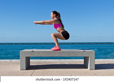 Hispanic woman doing squats on a bench by the ocean