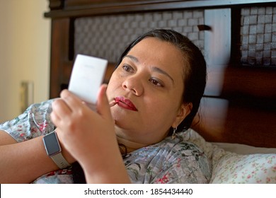 Hispanic Woman In Her 40s Putting On Makeup In Bed.