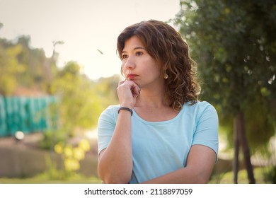 Hispanic Woman In Her 40s, Standing Thoughtful. Exteriors.