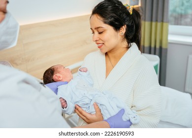 Hispanic Woman Holding Newborn Baby In Postnatal Hospital.