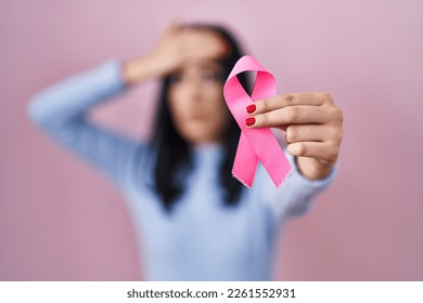 Hispanic woman holding pink cancer ribbon stressed and frustrated with hand on head, surprised and angry face  - Shutterstock ID 2261552931