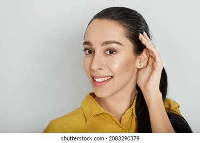 Hispanic Woman Holds Hand Near Her Ear For Listening To Ambient Sounds, On Grey Background. Adult Hearing Test Concept