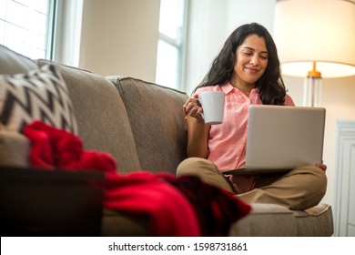 Hispanic woman at home working on a computer drinking coffee. - Powered by Shutterstock