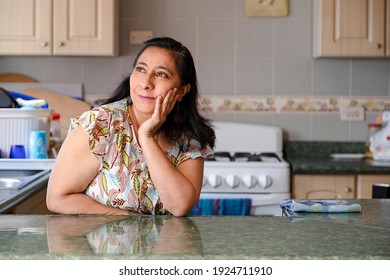 Hispanic Woman In The Kitchen Of Her Thinking-smiling Mom Dreaming Inspired In The Kitchen-Latina Woman Thinking That She Is Going To Cook