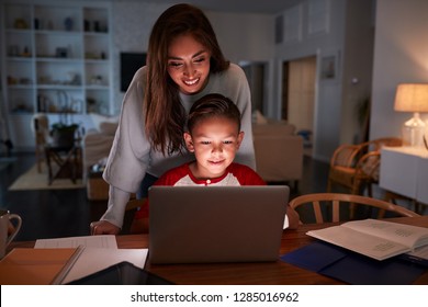 Hispanic Woman Looking Over Her SonÕs Shoulder While He Does His Homework Using Laptop Computer