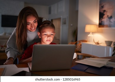 Hispanic Woman Looking Over Her SonÕs Shoulder While He Does His Homework Using Laptop Computer