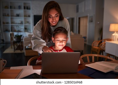 Hispanic Woman Looking Over Her SonÕs Shoulder While He Does His Homework Using Laptop Computer