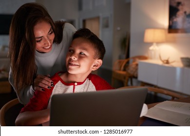 Hispanic Woman Looking Over Her SonÕs Shoulder While He Does His Homework Using Laptop Computer