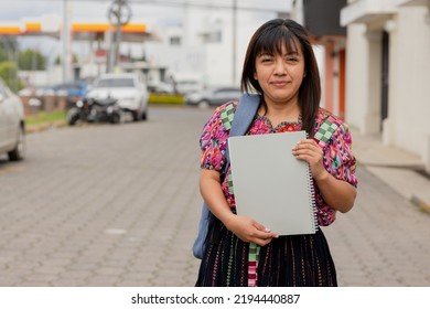 Hispanic woman with notebook and backpack outside school in the village - Mayan adult woman ready to go to study - Latina teacher - Shutterstock ID 2194440887