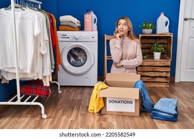 Hispanic Woman Putting Clothes In Donation Box Serious Face Thinking About Question With Hand On Chin, Thoughtful About Confusing Idea 