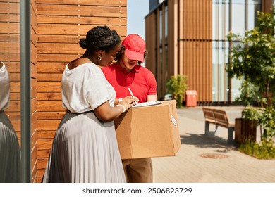 Hispanic woman receiving package from delivery man wearing red cap and uniform while standing outside modern building on sunny day - Powered by Shutterstock