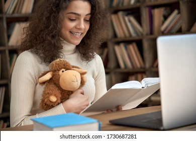 Hispanic Woman Remote Kids Teacher Reading Fairy Tale Book Teaching Online. Young Happy Latin Girl Holding Book And Toy Looking At Laptop Computer Webcam. Distance Children Video Call Zoom Education.