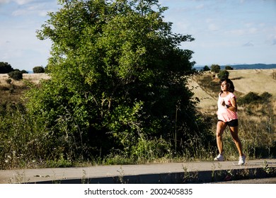 Hispanic Woman Running On A Country Road With Green Bush