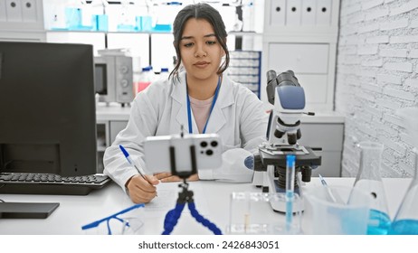 Hispanic woman scientist records video in lab with microscope and smartphone - Powered by Shutterstock