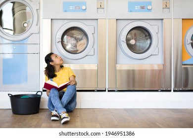 Hispanic woman sitting on the floor while waiting for clothes washing in the self-service laundry. Space for text. - Powered by Shutterstock