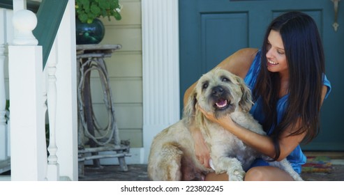 Hispanic Woman Sitting On Porch Scratching Dog