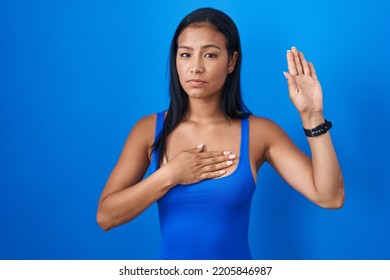 Hispanic Woman Standing Over Blue Background Swearing With Hand On Chest And Open Palm, Making A Loyalty Promise Oath 