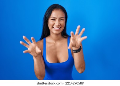 Hispanic Woman Standing Over Blue Background Smiling Funny Doing Claw Gesture As Cat, Aggressive And Sexy Expression 