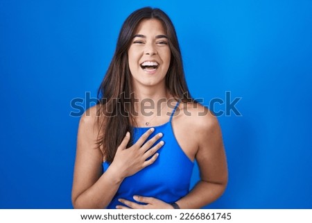 Hispanic woman standing over blue background smiling and laughing hard out loud because funny crazy joke with hands on body. 