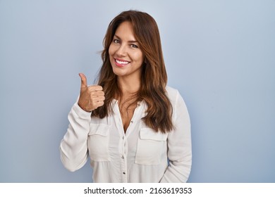 Hispanic woman standing over isolated background doing happy thumbs up gesture with hand. approving expression looking at the camera showing success. 