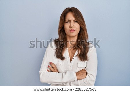 Hispanic woman standing over isolated background skeptic and nervous, disapproving expression on face with crossed arms. negative person. 