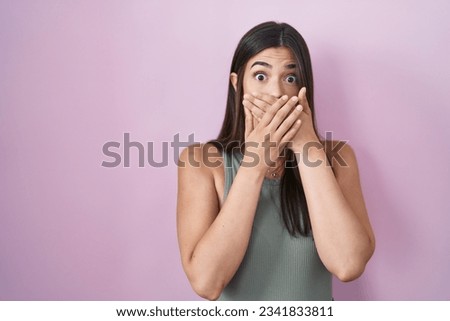 Hispanic woman standing over pink background shocked covering mouth with hands for mistake. secret concept. 