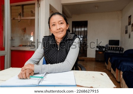 Hispanic woman studying at home - Happy senior adult writing in a notebook - Retired adult doing budgeting at home - Adult learning at home