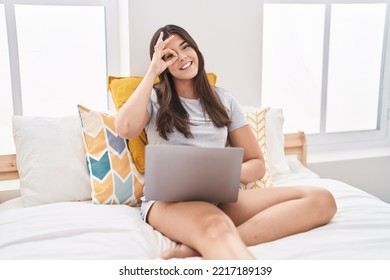 Hispanic Woman Using Computer Laptop On The Bed Smiling Happy Doing Ok Sign With Hand On Eye Looking Through Fingers 