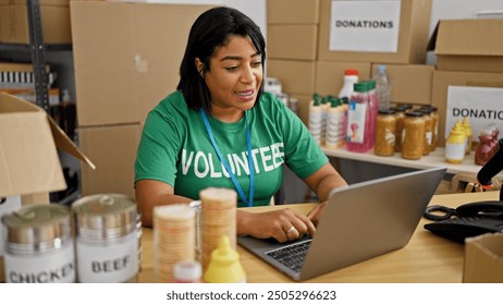 Hispanic woman volunteering at a donation center, organizing supplies and working on a laptop in a warehouse setting. - Powered by Shutterstock