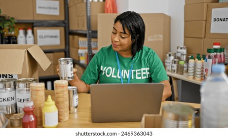 Hispanic woman volunteering at food bank using laptop among donations indoors. - Powered by Shutterstock