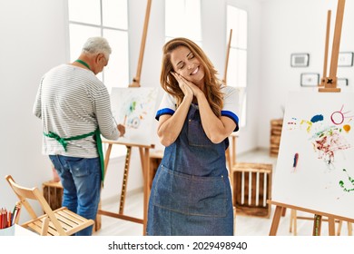 Hispanic woman wearing apron at art studio sleeping tired dreaming and posing with hands together while smiling with closed eyes.  - Powered by Shutterstock