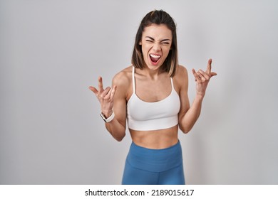 Hispanic Woman Wearing Sportswear Over Isolated Background Shouting With Crazy Expression Doing Rock Symbol With Hands Up. Music Star. Heavy Music Concept. 