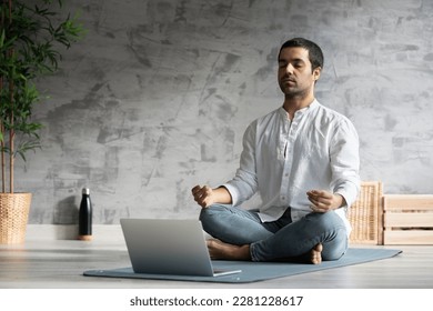 Hispanic yoga teacher meditating in front of laptop indoors. Student following meditation tutorial sitting on a mat - Powered by Shutterstock