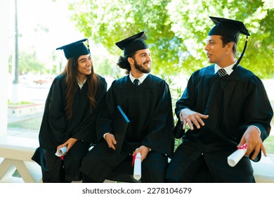 Hispanic young graduates chatting looking happy while sitting together after their graduation ceremony - Shutterstock ID 2278104679