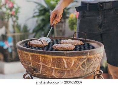 Hispanic Young Man Flipping Homemade Hamburgers Grilling At Backyard Bbq