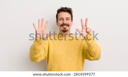 hispanic young man smiling and looking friendly, showing number eight or eighth with hand forward, counting down