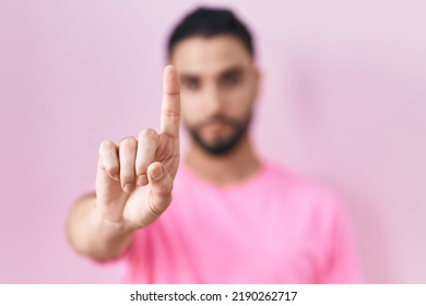 Hispanic Young Man Standing Over Pink Background Pointing With Finger Up And Angry Expression, Showing No Gesture 