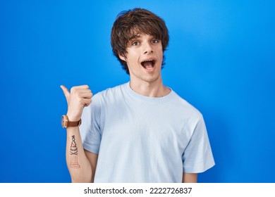 Hispanic Young Man Standing Over Blue Background With A Big Smile On Face, Pointing With Hand Finger To The Side Looking At The Camera. 