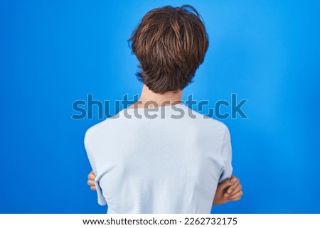 Hispanic young man standing over blue background standing backwards looking away with crossed arms 