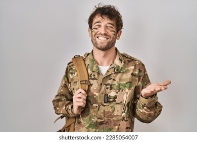 Hispanic young man wearing camouflage army uniform pointing aside with hands open palms showing copy space, presenting advertisement smiling excited happy  - Powered by Shutterstock