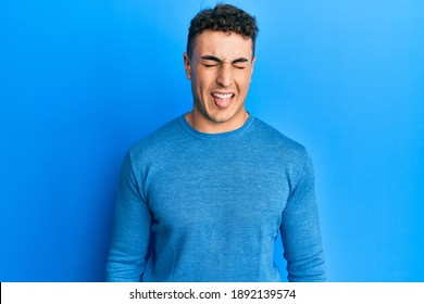 Hispanic young man wearing casual winter sweater sticking tongue out happy with funny expression. emotion concept.  - Shutterstock ID 1892139574